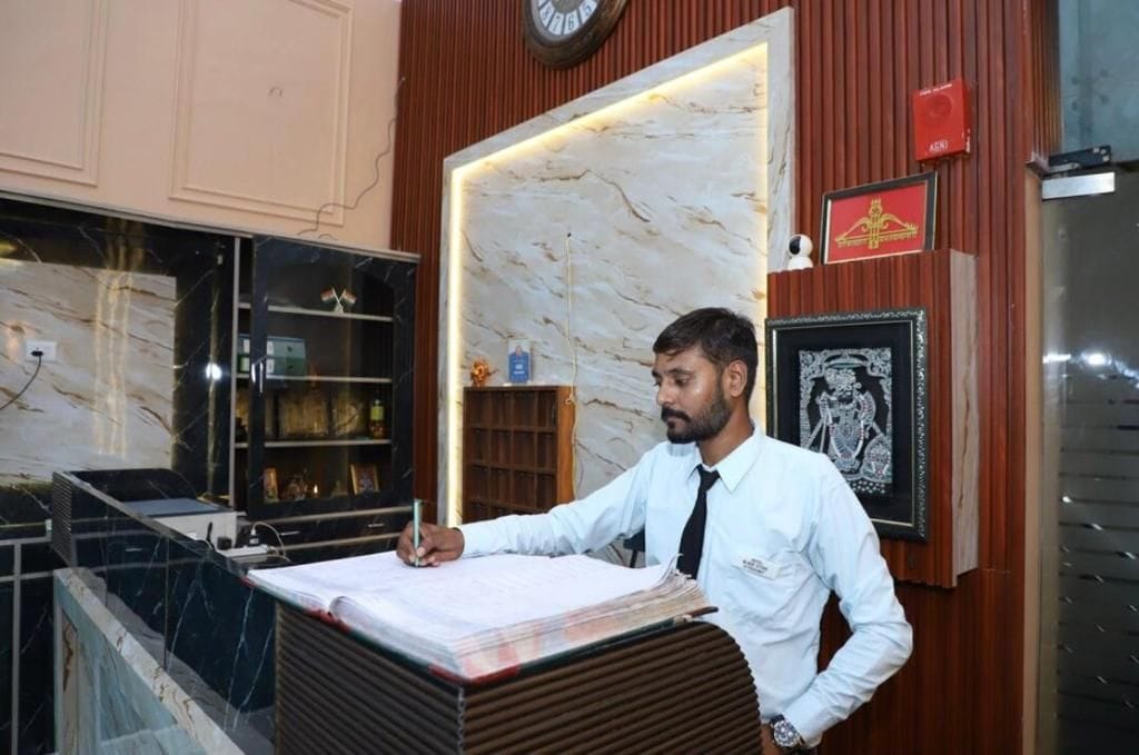 Un hombre en la recepción de un hotel, con paredes de mármol, un reloj y obras de arte enmarcadas.
