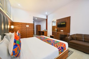 Quarto de hotel com cama, sofá, televisão e escrivaninha.