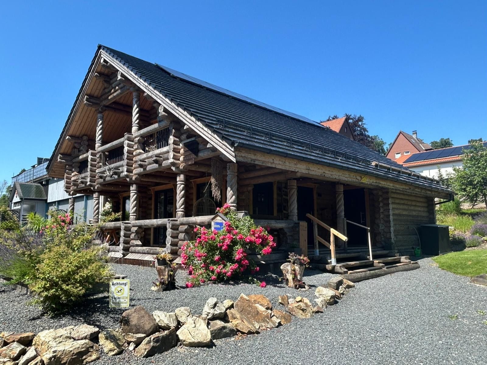 Eine Blockhütte mit Veranda, umgeben von einer Schotterauffahrt und einem Felsengarten.