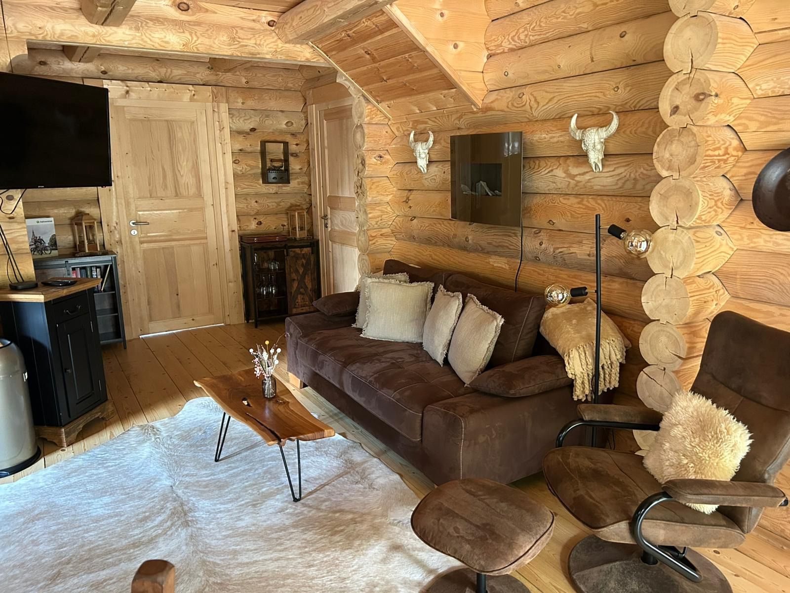 Ein gemütliches Blockhaus-Interieur mit einer Holzwand, einem braunen Ledersofa, einem Holztisch und einem flauschigen Teppich.