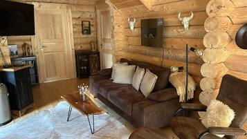 Ein gemütliches Blockhaus-Interieur mit einer Holzwand, einem braunen Ledersofa, einem Holztisch und einem flauschigen Teppich.