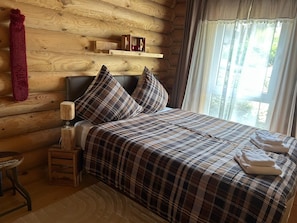 Une chambre confortable dans un chalet en rondins, avec un lit, une table de chevet, une lampe et une fenêtre avec des rideaux.