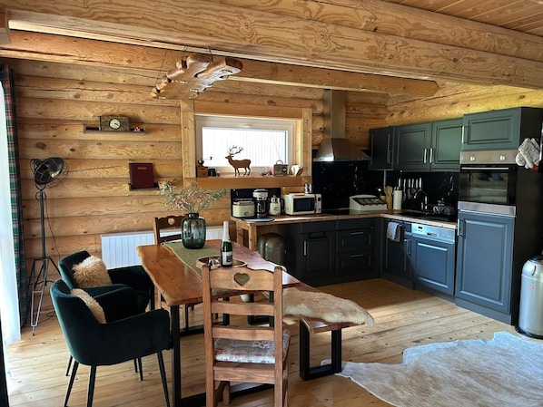 Un intérieur en bois comprenant une table à manger, des chaises, une cuisine équipée et un luminaire au plafond.