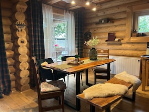 Un intérieur en bois comprenant une table à manger, des chaises, un banc, un vase avec des fleurs et une horloge au mur.