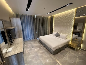 Un dormitorio moderno con una cama, un tocador con espejo y un televisor montado en la pared.