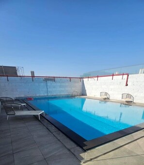 A swimming pool with a clear blue water surface, surrounded by a white tiled wall, and equipped with lounge chairs and a red safety railing. - Mirada Gold - Obhur (Jeddah)