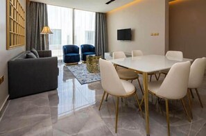 A modern hotel room with a dining area, a sofa, and a TV mounted on the wall.