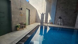 Une piscine à l’eau d’un bleu cristallin, entourée de murs en pierre et dotée d’une porte sur laquelle est inscrit « Zone piscine ».