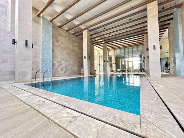 An indoor swimming pool with clear water, surrounded by stone walls and wooden beams.