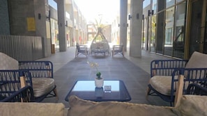 A covered outdoor seating area with wicker chairs and a glass-top table, featuring a potted plant.
