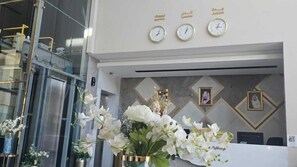Un espace d’accueil avec un bureau, une horloge et des tableaux encadrés accrochés au mur.