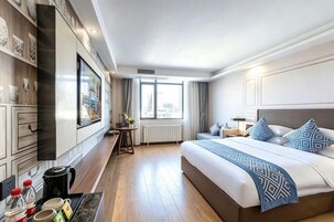 Habitación de hotel con cama, mesita de noche, lámpara y vistas a la ciudad a través de una ventana.