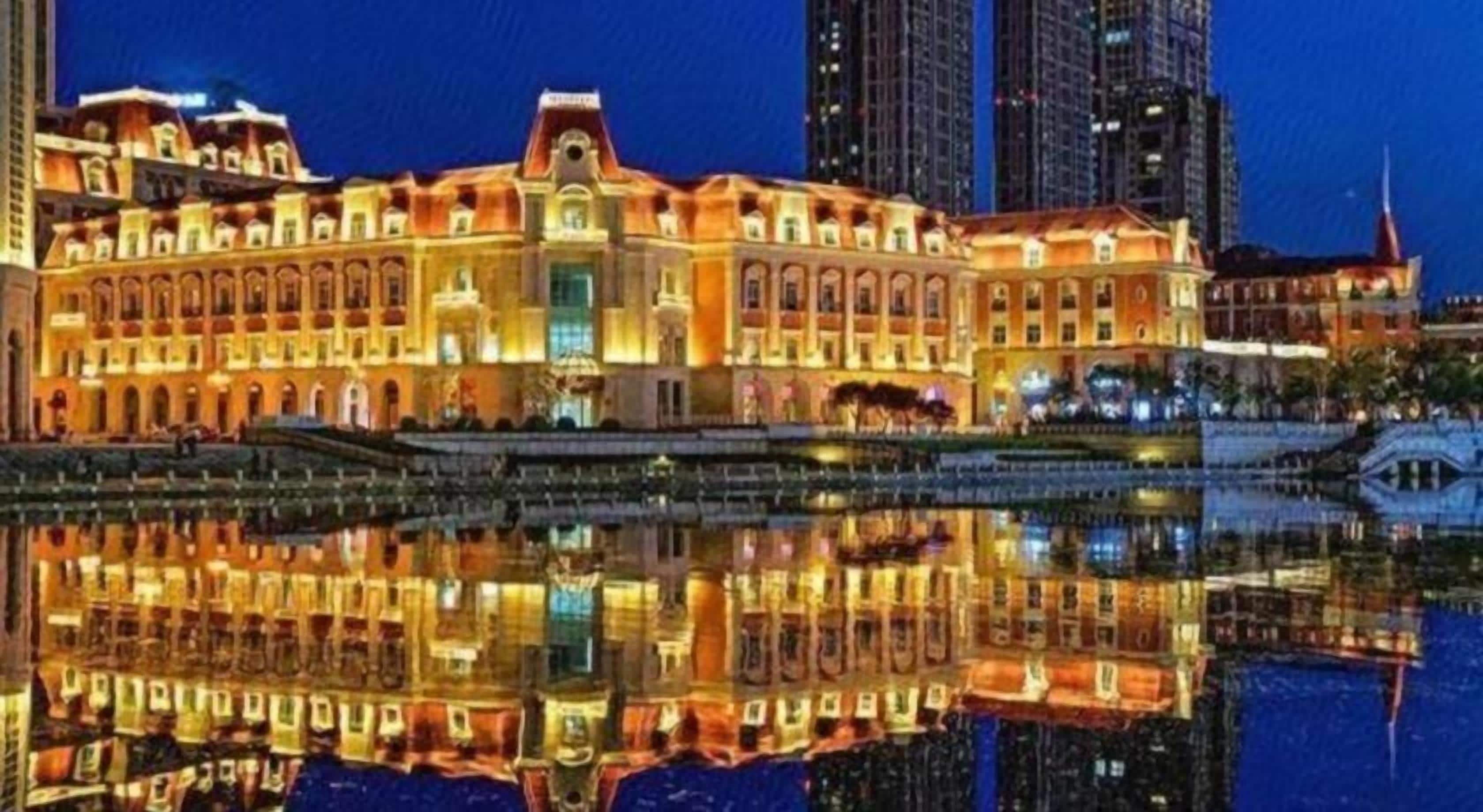 A hotel with a reflection in the water, featuring a classical architectural style with multiple stories and a prominent entrance.