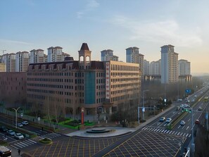 A multi-story building with a central tower, surrounded by other high-rise buildings. - Vienna 3 Best Hotel (Tianjin)