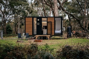 A mobile home with a kitchen area, a sleeping area, and a small outdoor seating space. - Cozy Tiny House with Barbecue, Firepit and River Views in Victoria, Australia (Dadswells Bridge)