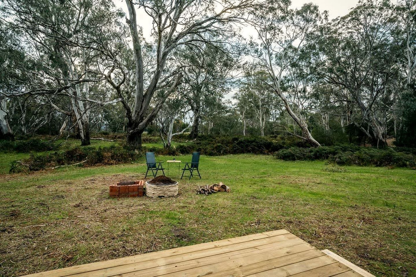 Une terrasse en bois avec deux chaises et une table, entourée d’une pelouse et de quelques arbres.