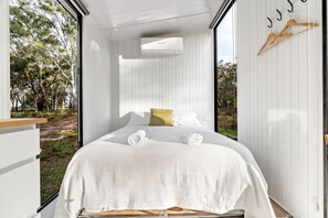 A bedroom with a bed, white walls, a window, and a view of trees.