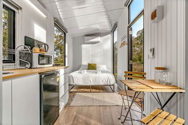 A compact bedroom with a bed, bedside table, and a view of the outdoors.