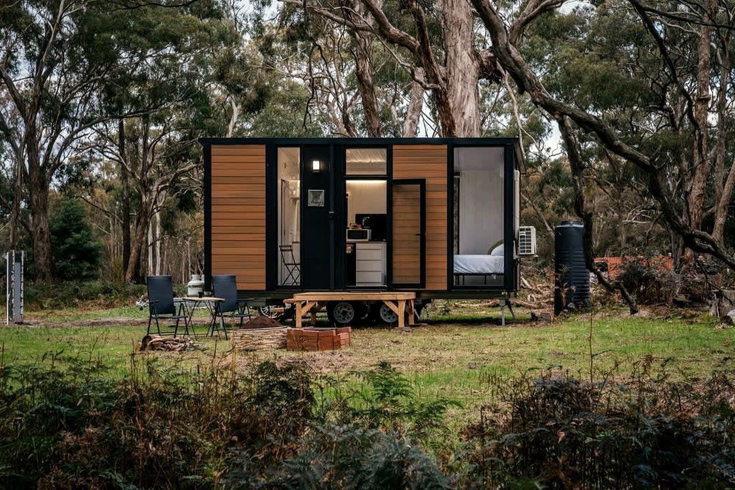 Una casa móvil con zona de cocina, zona de descanso y un pequeño espacio con mobiliario de exterior.