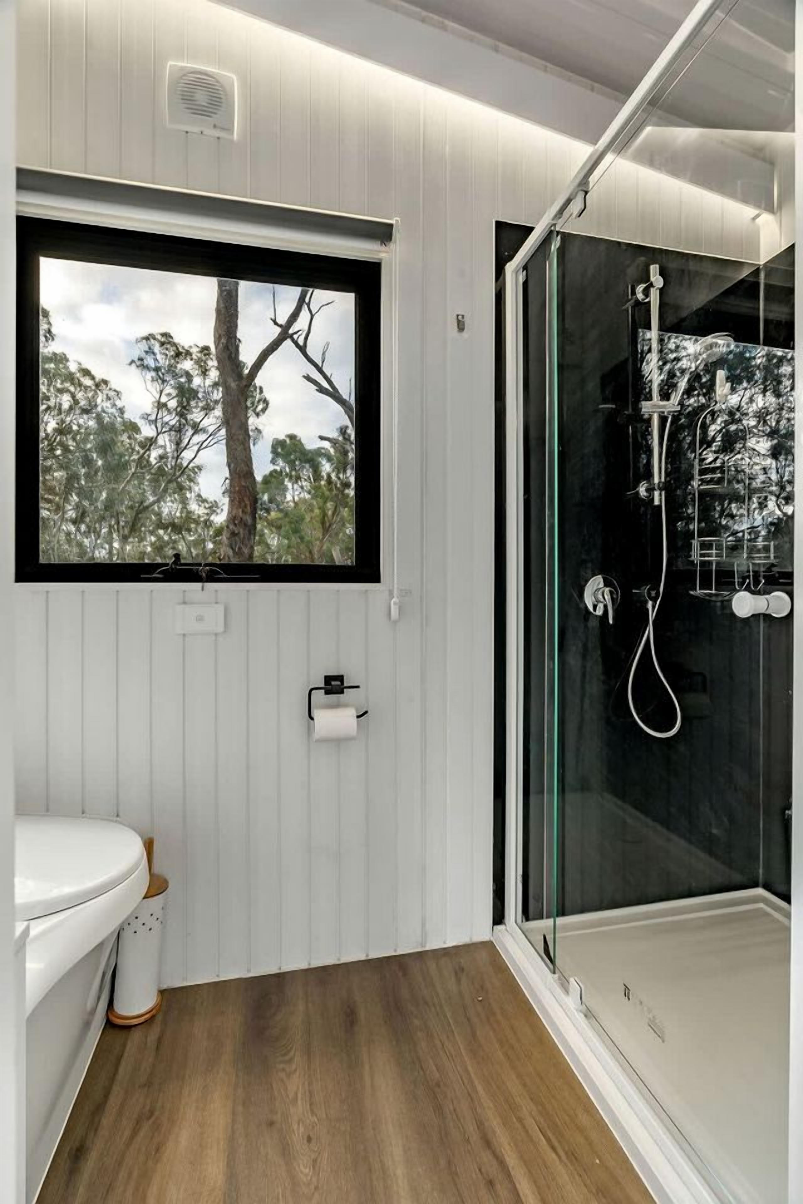 A bathroom with a toilet, a window with a view of trees, and a glass-enclosed shower area.