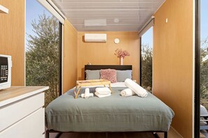 A compact bedroom with a bed, bedside table, and a window. - Serene Tiny House with Amazing Countryside Landscapes in New South Wales (West Wyalong)