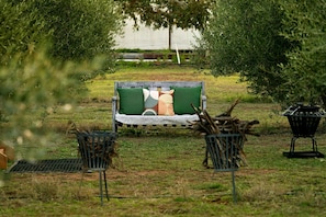 Un espace extérieur aménagé avec un banc et deux chaises, entouré de verdure.