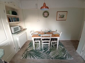 A dining area with a wooden table, white chairs, and a patterned rug. - Hafan (Criccieth)