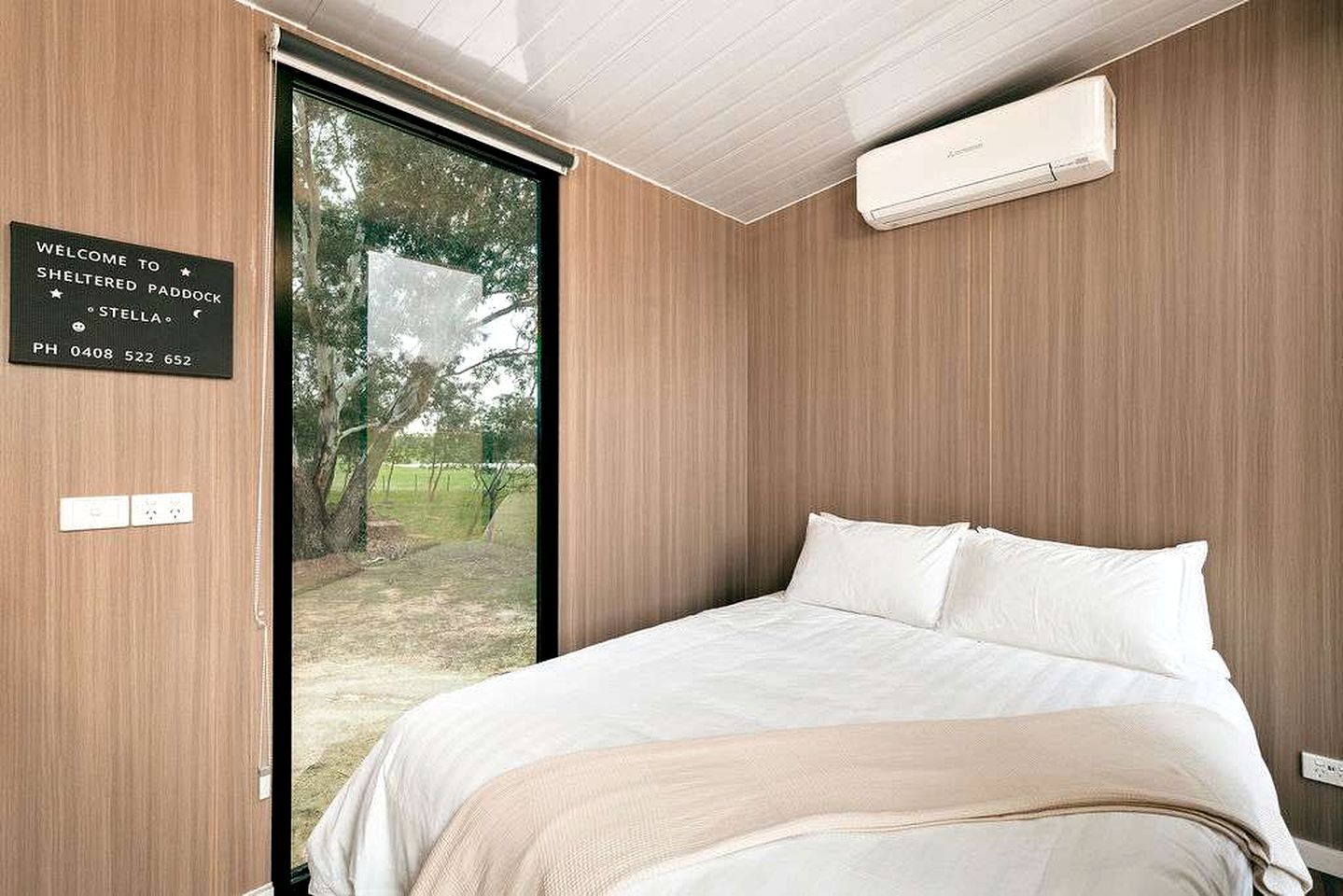Quarto moderno com uma cama grande, vista para o exterior e uma placa de boas-vindas.