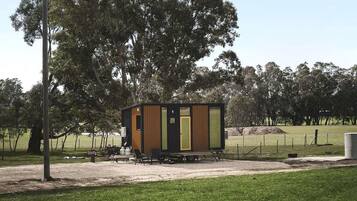 A small, modern cabin with a wooden exterior, a door, and a bench outside.
