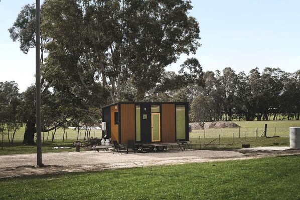A small, modern cabin with a wooden exterior, a door, and a bench outside. - Cozy Off-Grid Tiny House Farm Stay with Wildlife Views near Pyrenees Wine Region, Warrenmang Victoria (Warrenmang)