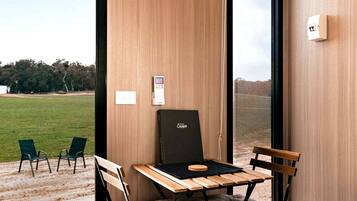 A room with a wooden table, two chairs, a black chair, and a view of a grassy field through a window.