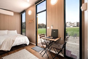 A modern bedroom with a bed, a desk, and a laptop, featuring large windows and a view of a grassy area. - Cozy Off-Grid Tiny House Farm Stay with Wildlife Views near Pyrenees Wine Region, Warrenmang Victoria (Warrenmang)
