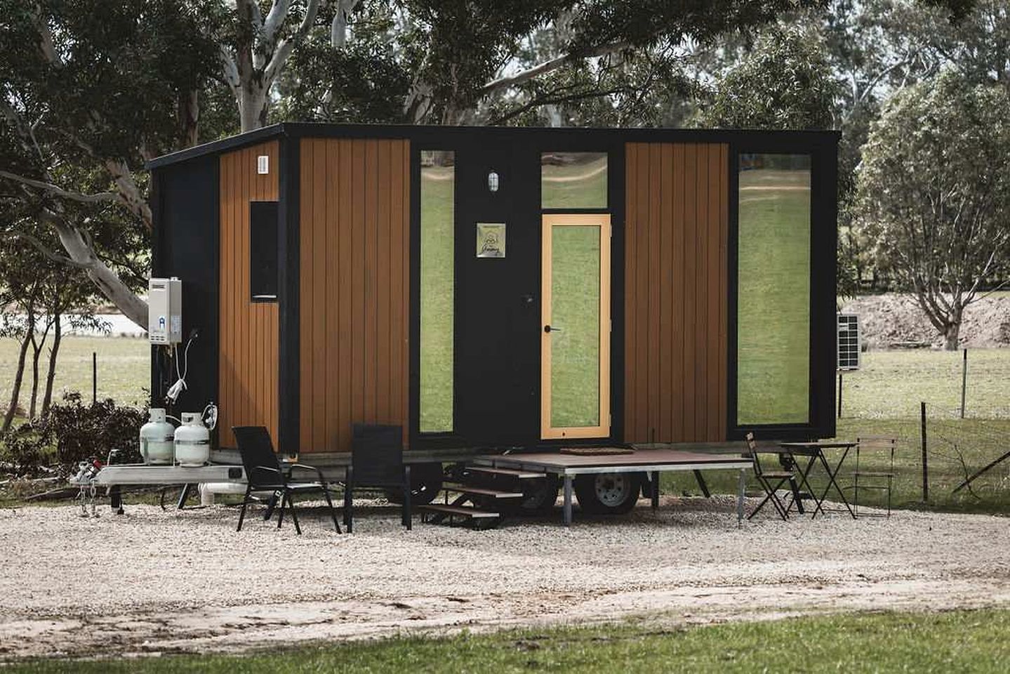 Een klein, gelijkvloers blokhutje met een voordeur, een raam en een tafel met stoelen ervoor.