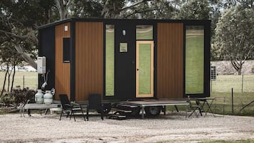 Een klein, gelijkvloers blokhutje met een voordeur, een raam en een tafel met stoelen ervoor.
