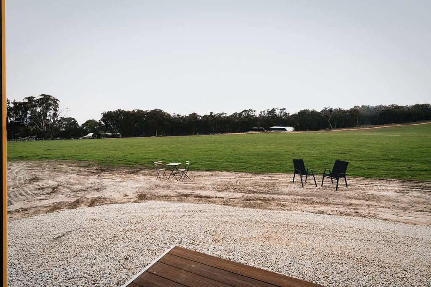 A gravel area with a wooden deck, two green folding chairs, and a table.