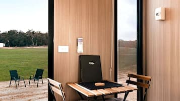 Een kamer met een houten tafel, twee stoelen, een zwarte stoel en uitzicht op een grasveld door een raam.