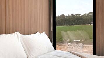 A bedroom with a large window, a bed, and a view of an outdoor area with chairs.