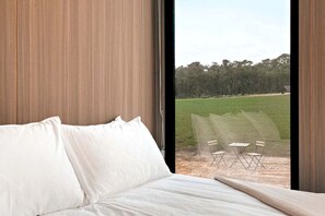 A bedroom with a large window, a bed, and a view of an outdoor area with chairs.