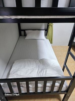 Una cama individual con colchón y almohadas blancos, una cortina verde y un marco de metal negro.