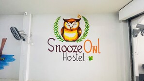 Una pared con el logotipo del 'Snooze Owl Hostel', que presenta un búho y una corona de laurel.