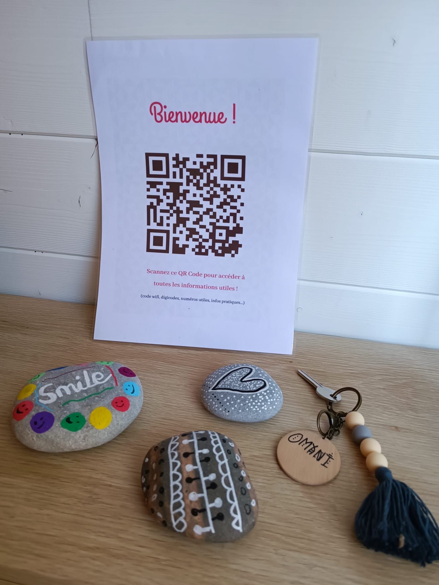 Un letrero de bienvenida con un código QR, un llavero y tres piedras decoradas.
