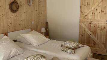 Un dormitorio con pared de listones de madera, cama con ropa de cama blanca, lámpara de techo trenzada y un banco de madera.
