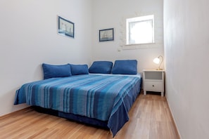 A bedroom with a bed, blue pillows, a nightstand with a lamp, and two framed pictures on the wall. - Chic apartment in center of Split (Split)