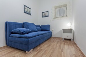 A room with a blue sofa, a white nightstand with a lamp, and two framed pictures on the wall. - Chic apartment in center of Split (Split)
