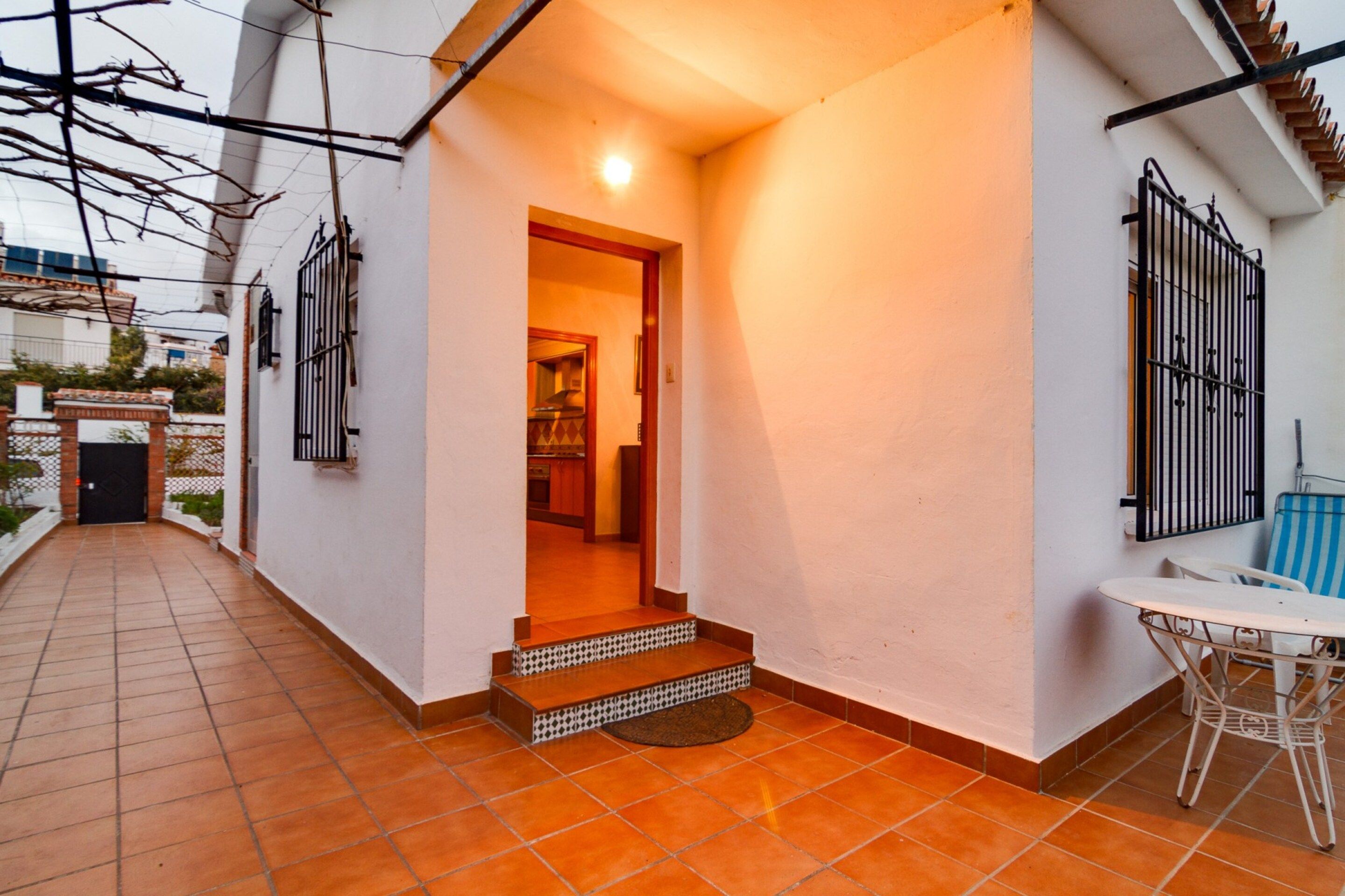 A residential property with a tiled patio, a small outdoor seating area, and a visible kitchen entrance.