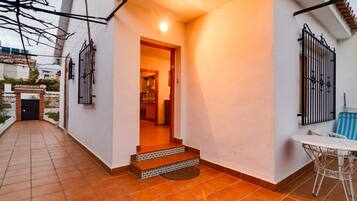 A residential property with a tiled patio, a small outdoor seating area, and a visible kitchen entrance.