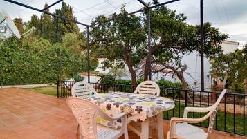 An outdoor patio with a table and chairs, surrounded by a metal fence and trees.