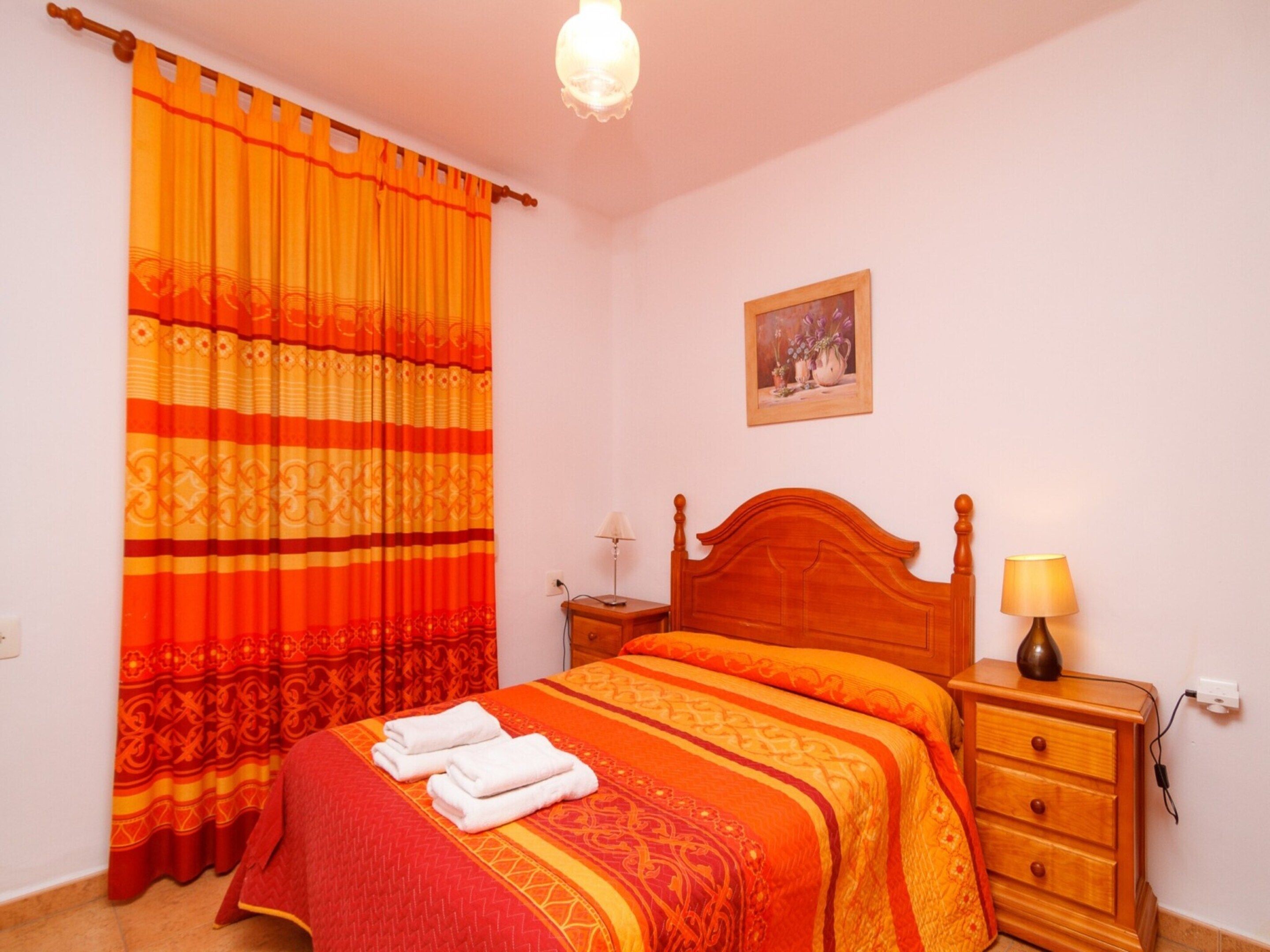 A bedroom with a bed, a nightstand, a lamp, and a painting on the wall.
