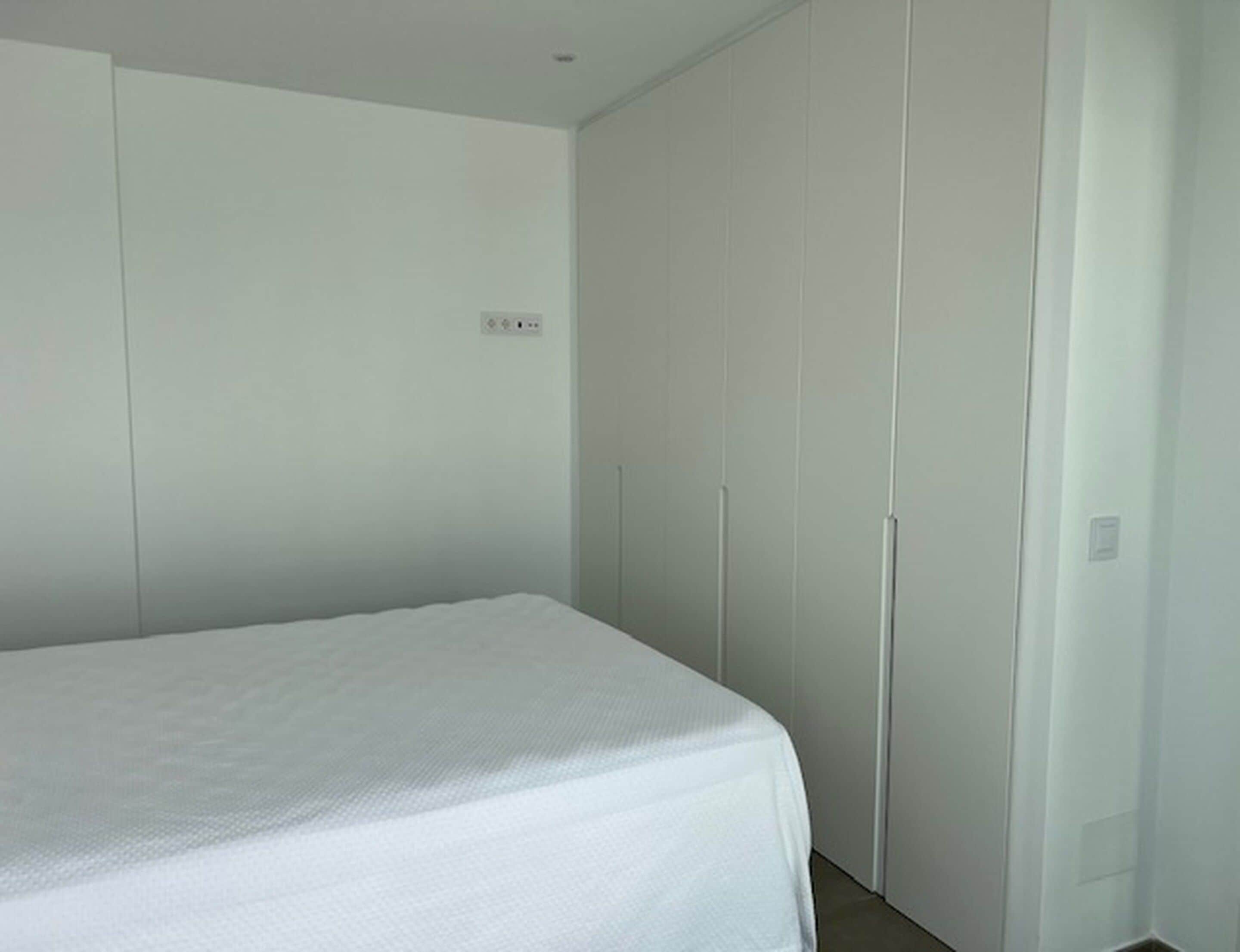 A bedroom with a single bed, a wardrobe, and a small wall-mounted shelf.