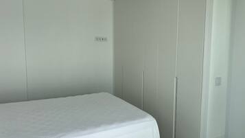 A bedroom with a single bed, a wardrobe, and a small wall-mounted shelf.